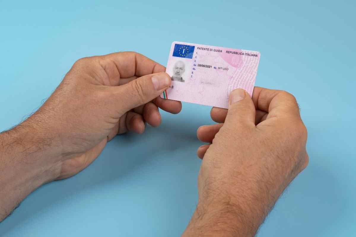 mani stringono una patente tra le dita